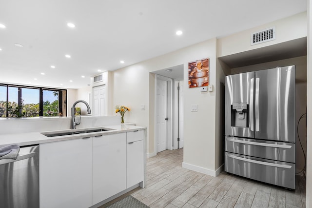 kitchen featuring visible vents, light wood-style flooring, appliances with stainless steel finishes, white cabinets, and a sink