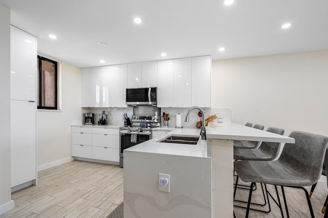 kitchen with a peninsula, a sink, stainless steel appliances, a kitchen bar, and modern cabinets