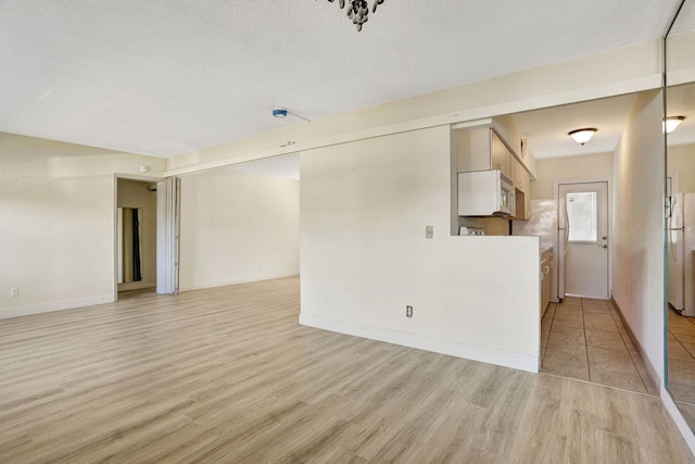 3212 NE 8th Ct Unit 7, Pompano Beach, FL 33062 - unfurnished living room with light wood finished floors, baseboards, and a textured ceiling