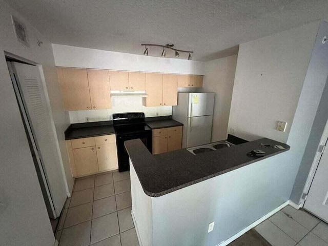 kitchen featuring dark countertops, under cabinet range hood, a peninsula, freestanding refrigerator, and black electric range