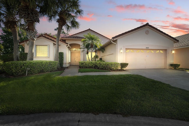 view of front of property with a tile roof, stucco siding, driveway, a garage, and a lawn