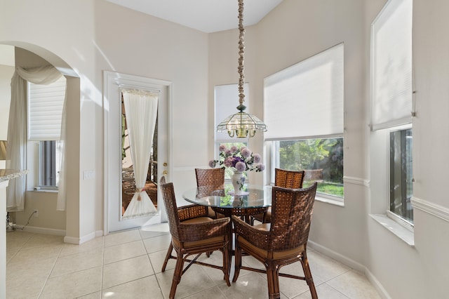 dining space featuring an inviting chandelier, light tile patterned floors, arched walkways, and baseboards