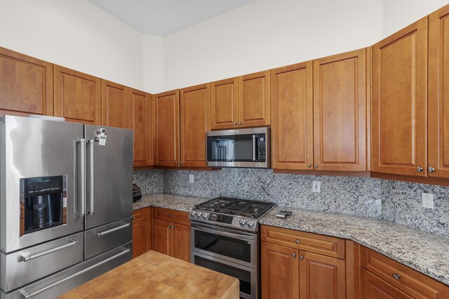 kitchen with tasteful backsplash, appliances with stainless steel finishes, and light stone counters