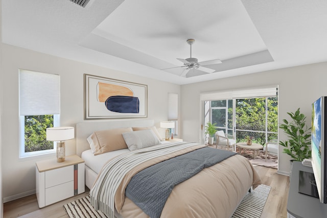 bedroom with a tray ceiling, light wood-type flooring, baseboards, access to outside, and ceiling fan