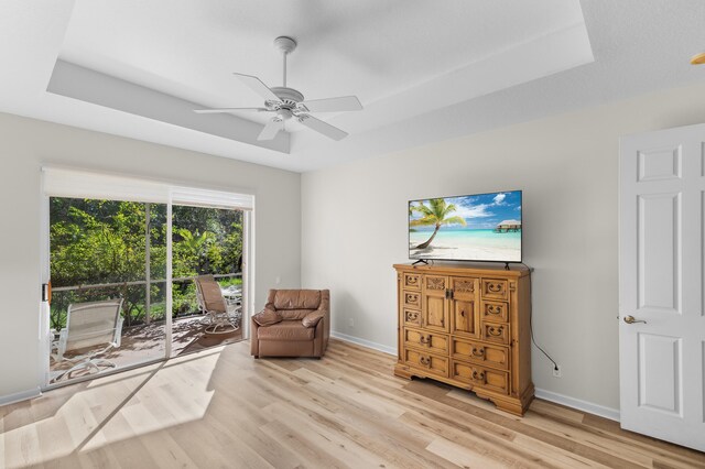 living area featuring a ceiling fan, a raised ceiling, baseboards, and light wood finished floors