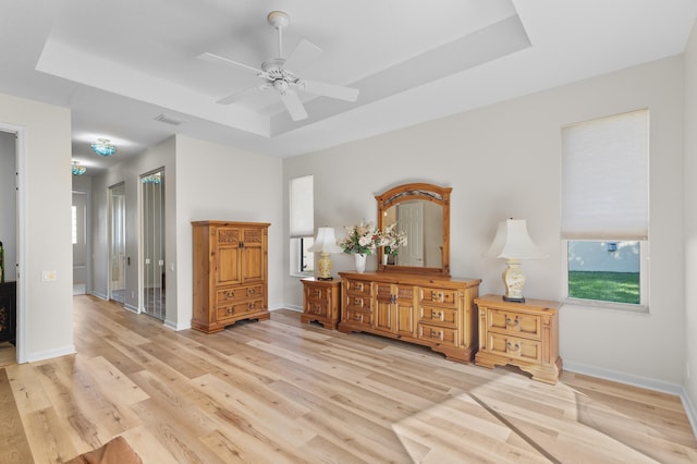 bedroom with baseboards, light wood-type flooring, visible vents, and a raised ceiling