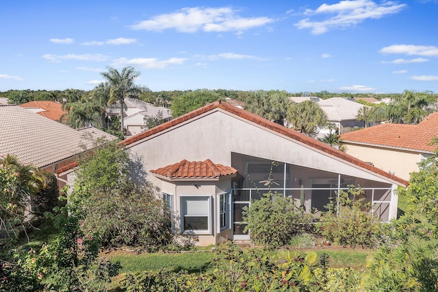 rear view of property featuring a tile roof, stucco siding, and a sunroom