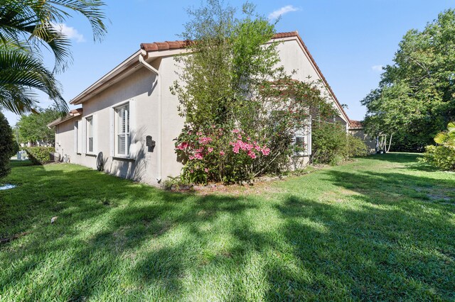 view of side of property featuring stucco siding, a tile roof, and a yard