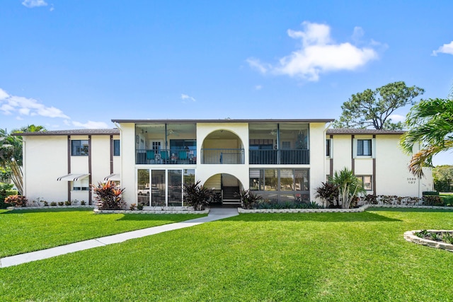 rear view of property with stucco siding, a yard, a ceiling fan, and a sunroom