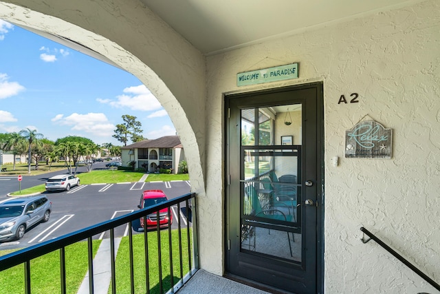 property entrance with stucco siding, a balcony, and uncovered parking
