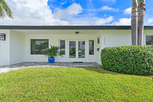rear view of property with french doors, a yard, and stucco siding