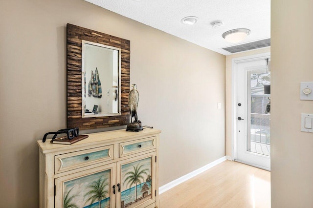 interior space with visible vents, a textured ceiling, light wood-type flooring, and baseboards
