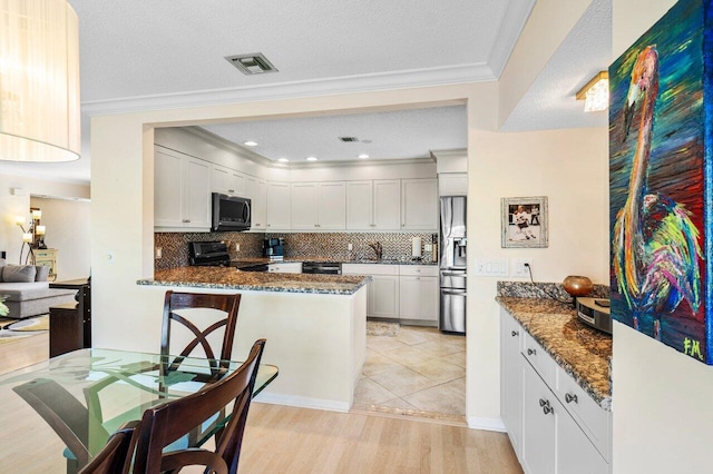 kitchen featuring visible vents, dark stone counters, a peninsula, ornamental molding, and stainless steel appliances