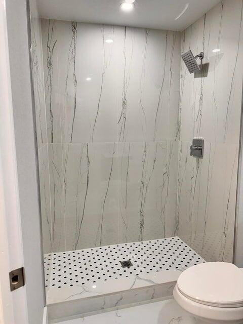 bathroom featuring a marble finish shower and toilet