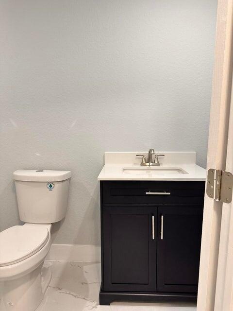 bathroom with vanity, baseboards, toilet, a textured wall, and marble finish floor
