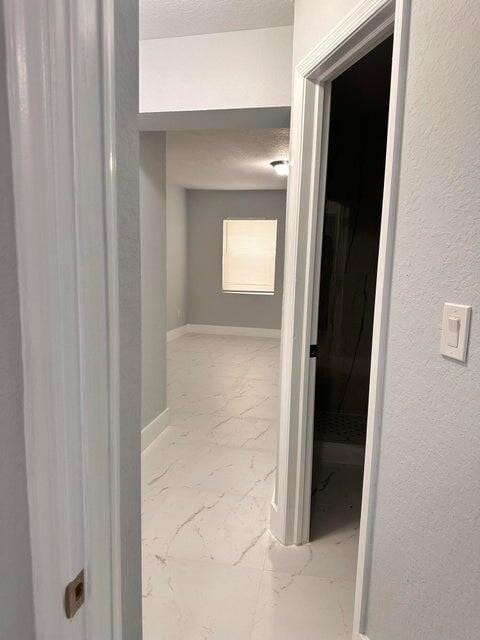 hall featuring marble finish floor, a textured ceiling, and baseboards