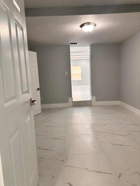empty room with marble finish floor, a textured ceiling, and baseboards