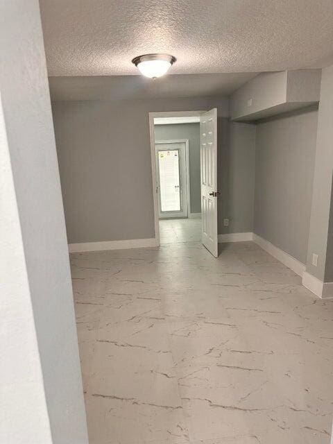 spare room with marble finish floor, a textured ceiling, and baseboards
