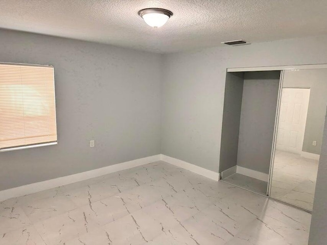 unfurnished bedroom featuring visible vents, marble finish floor, a textured ceiling, a closet, and baseboards