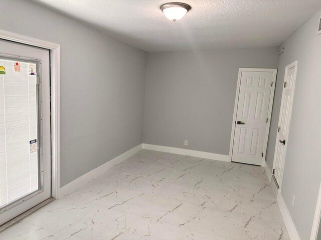 empty room with baseboards, marble finish floor, and a textured ceiling
