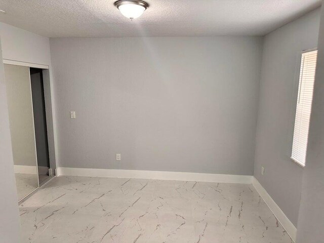 empty room with baseboards, marble finish floor, and a textured ceiling