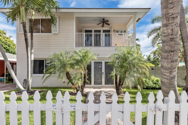 view of front of home with a balcony, a fenced front yard, ceiling fan, and french doors