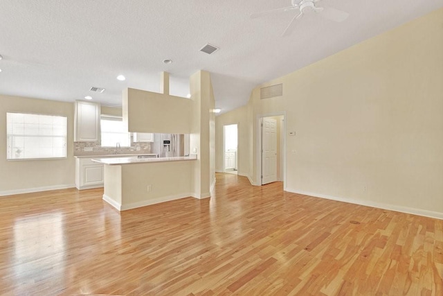 unfurnished living room featuring light wood-style floors, ceiling fan, baseboards, and a textured ceiling