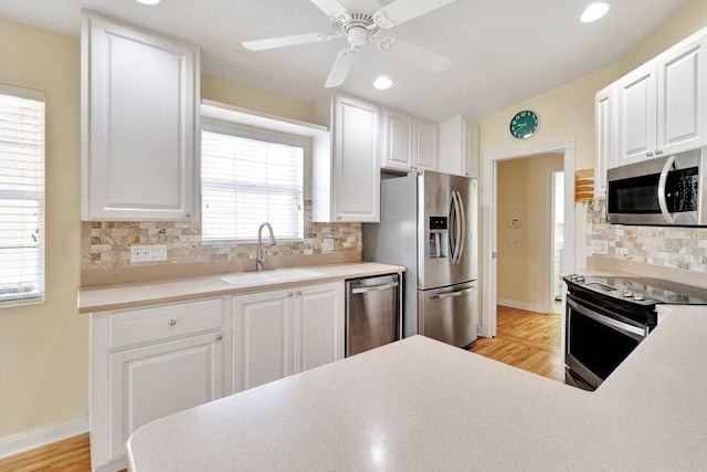 kitchen with appliances with stainless steel finishes, a sink, light wood-style flooring, backsplash, and white cabinetry