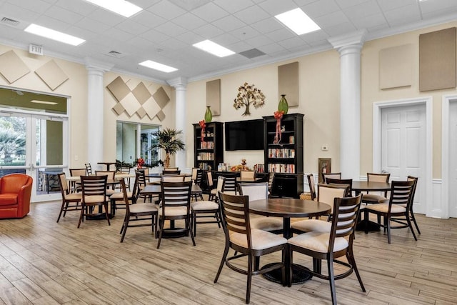 dining space with decorative columns, a towering ceiling, ornamental molding, and light wood-type flooring