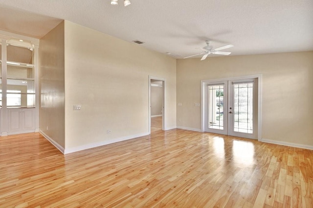 empty room with light wood-type flooring, ceiling fan, baseboards, a textured ceiling, and french doors