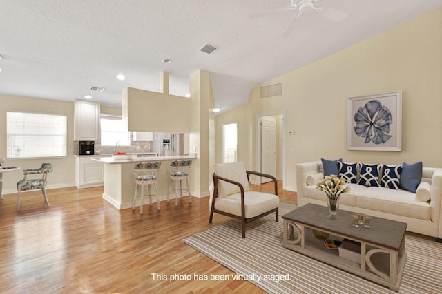 living area with light wood-style flooring, ceiling fan, baseboards, a textured ceiling, and vaulted ceiling