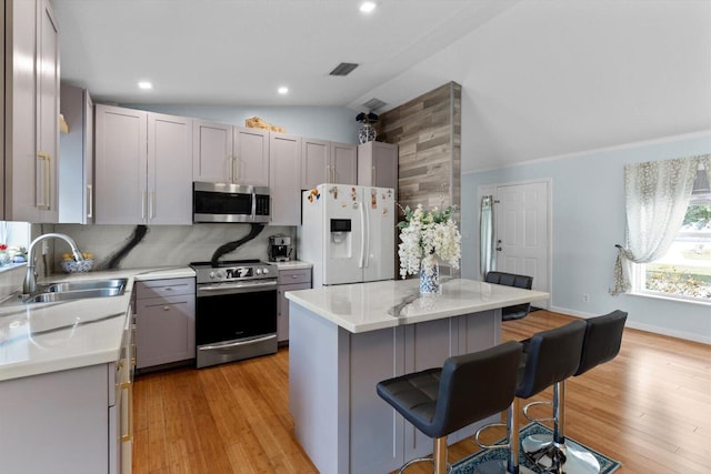 kitchen featuring visible vents, a breakfast bar, gray cabinets, appliances with stainless steel finishes, and a sink