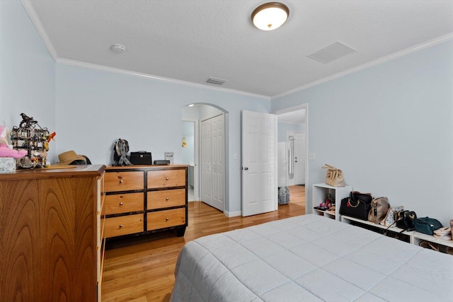 bedroom with crown molding, light wood-style flooring, visible vents, and arched walkways