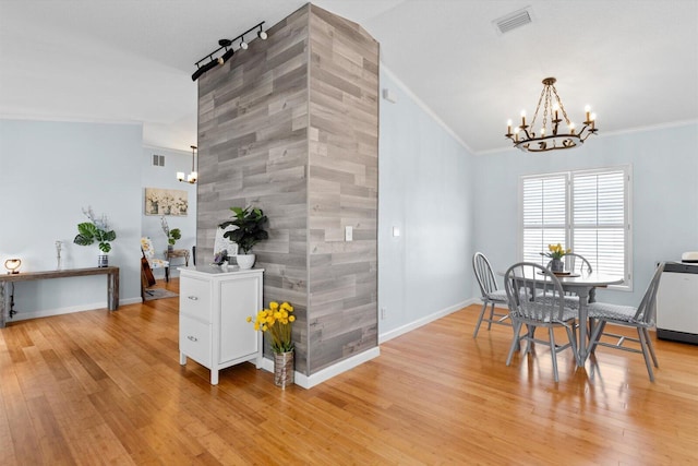 dining room with light wood finished floors, crown molding, an accent wall, baseboards, and a chandelier