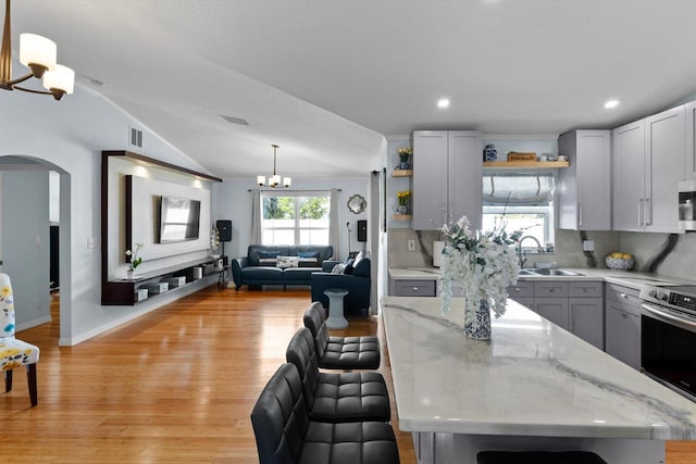 kitchen featuring an inviting chandelier, open shelves, arched walkways, a sink, and stainless steel appliances