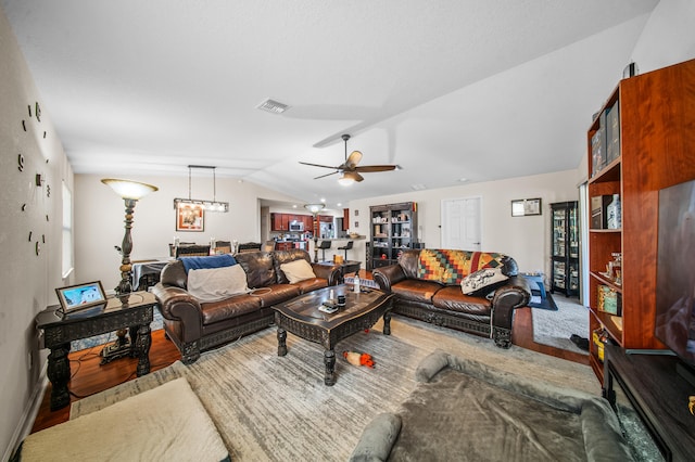 living area featuring visible vents, ceiling fan with notable chandelier, lofted ceiling, and wood finished floors