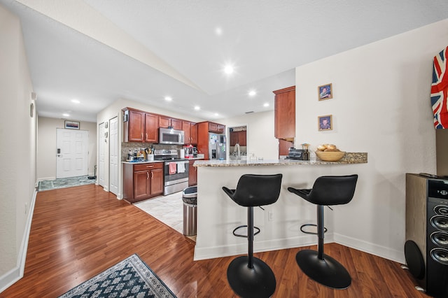 kitchen featuring backsplash, stainless steel appliances, a peninsula, light wood finished floors, and vaulted ceiling