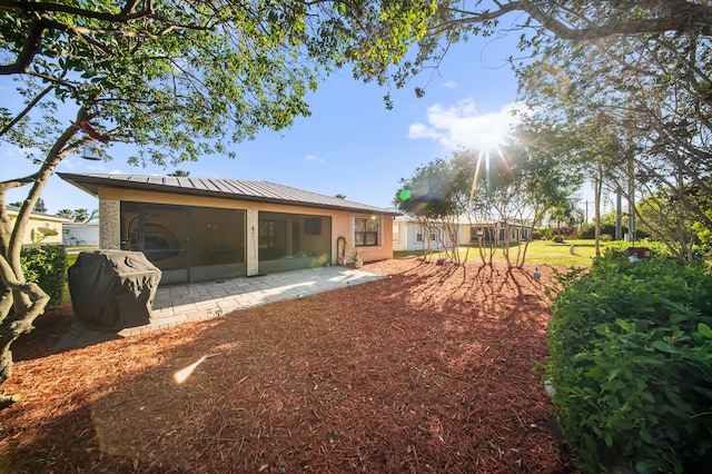 rear view of house with a patio, stucco siding, a sunroom, and metal roof