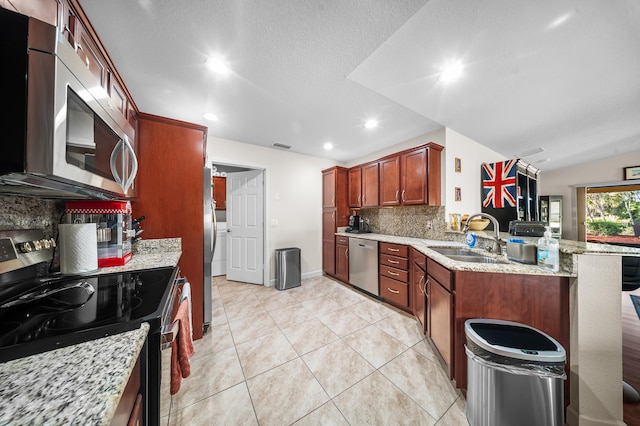 kitchen with light stone counters, decorative backsplash, a peninsula, stainless steel appliances, and a sink