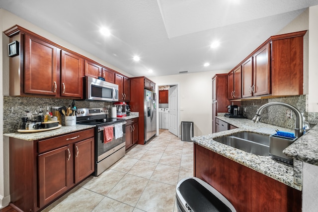 kitchen featuring a sink, separate washer and dryer, light stone countertops, and stainless steel appliances