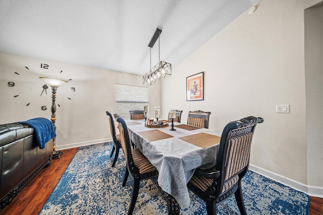 dining area with baseboards, a textured ceiling, wood finished floors, and vaulted ceiling