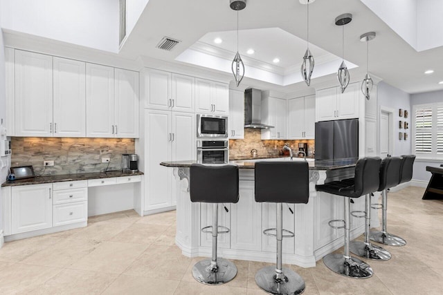 kitchen with visible vents, wall chimney range hood, appliances with stainless steel finishes, white cabinets, and a raised ceiling