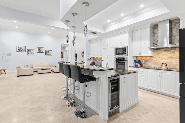kitchen with wine cooler, appliances with stainless steel finishes, a raised ceiling, and wall chimney range hood