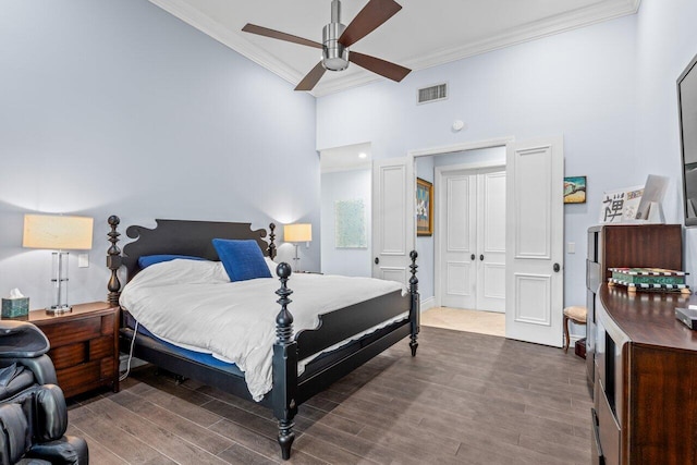 bedroom with a high ceiling, wood finished floors, visible vents, and ornamental molding
