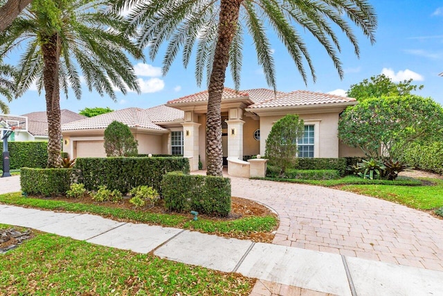 mediterranean / spanish-style home featuring stucco siding, a tiled roof, an attached garage, and curved driveway