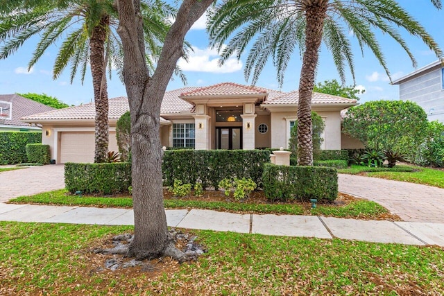mediterranean / spanish house featuring stucco siding, a tile roof, decorative driveway, and a garage