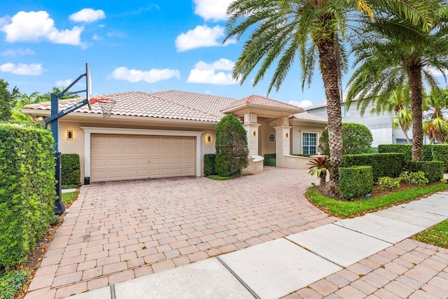 mediterranean / spanish-style home featuring stucco siding, a tile roof, decorative driveway, and a garage