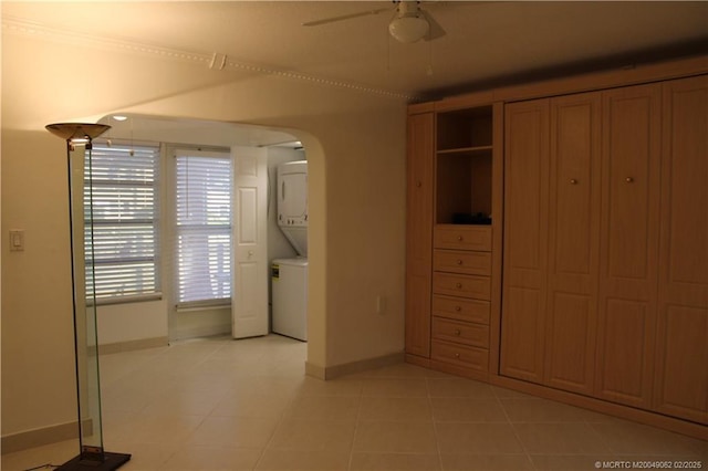 unfurnished bedroom featuring light tile patterned flooring, arched walkways, stacked washer / drying machine, and baseboards