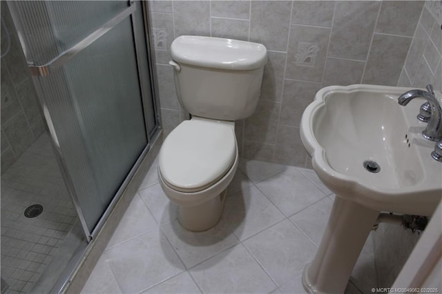 bathroom with toilet, a stall shower, tile patterned floors, tile walls, and a sink