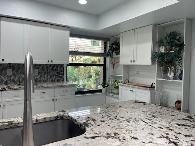 kitchen with light stone counters, white cabinets, tasteful backsplash, and a sink